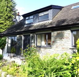 Exterior view of a stone and wood house with front door windows and a garden with various plants and shrubs at Wysteria Cottage in Windermere