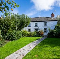 A stone path leading to a white cottage with a garden and green bushes at Fern Cottage in Aberporth