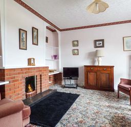 A living room with a brick fireplace a TV armchairs and a wooden cabinet at Glenhaven in Sweffling near Snape