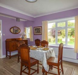 A dining room with a wooden table and chairs near large windows at Glenhaven in Sweffling near Snape