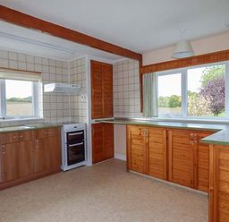 A kitchen with wooden cabinets a white oven and large windows overlooking a field at Glenhaven in Sweffling near Snape