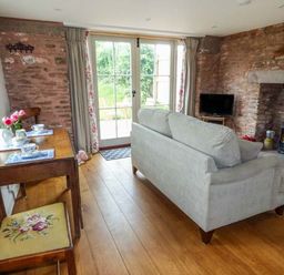 A living room with a sofa a wooden table with chairs a fireplace and a TV at Rose Cottage in Welsh Newton