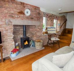 A living room with a wood burning stove fireplace rocking chair sofa and TV at Rose Cottage in Welsh Newton