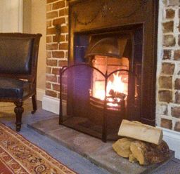 A fireplace with firewood and fireguard beside a chair on a carpet at Woodland Cottage in Malvern