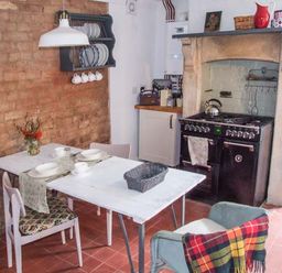 A kitchen with a white table set with dishes a brick wall a stove and chairs with a blanket at Woodland Cottage in Malvern