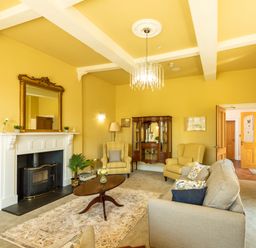 A living room with yellow walls a fireplace two armchairs a sofa a wooden coffee table and a cabinet at Old Rectory House Caersws