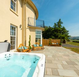 An outdoor patio with a hot tub wooden benches with cushions and a view of trees and fields at Old Rectory House in Caersws