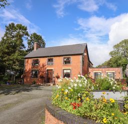 A brick house with a driveway and flower bed in front at Ty Newydd in Llangadfan