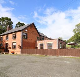 A brick house with a slate roof and brown wooden fence in front with trees and patio umbrellas at Ty Newydd in Llangadfan