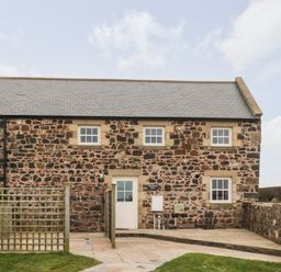 Exterior view of a stone house with six windows a door and a small fenced paved area at High Hemmel House in Embleton