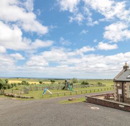 A playground with slides and benches near a brick building in an open field at Home Stead Cottage in Embleton