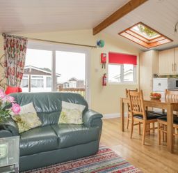 A living area with a green leather sofa and a wooden dining table with chairs near a kitchen at Tiggy Winkle in St Merryn near Padstow