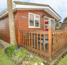 Exterior of a wooden cabin with a small fenced porch and garden at Tiggy Winkle in St Merryn near Padstow