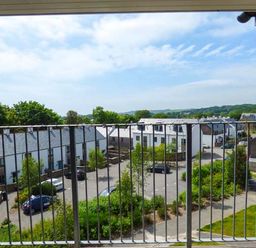 A balcony with metal railing overlooking a residential area with white houses and parked cars at Tehidy in Charlestown