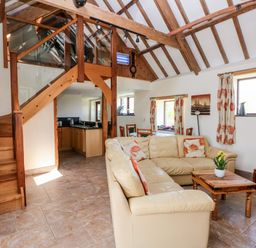 A living room with a beige sectional sofa and wooden coffee table next to a staircase and kitchen at The Long Barn in Hasguard near Little Haven
