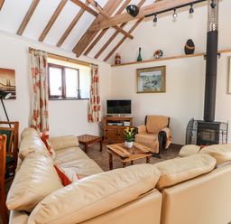 A living room with a cream sectional sofa a wooden coffee table an armchair wood stove and TV at The Long Barn in Hasguard near Little Haven
