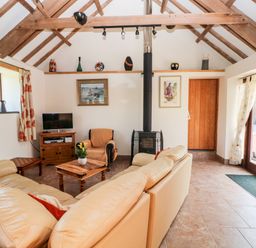 A living room with beige sofas a wooden coffee table a wood stove a TV on a wooden stand and exposed wooden beams at The Long Barn in Hasguard near Little Haven