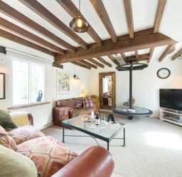 A living room with wooden beams on the ceiling a glass coffee table leather sofas a wall mirror a television and a round hanging shelf at Grafton Mill in Grafton Flyford near Pershore
