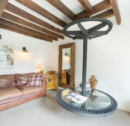 A living room with a brown leather sofa a wooden side table a large mirror a round glass coffee table and a wall clock at Grafton Mill in Grafton Flyford near Pershore