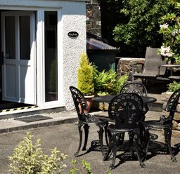 An outdoor patio with a black metal table and four chairs near a white door at Kingfisher in Blaenwaun