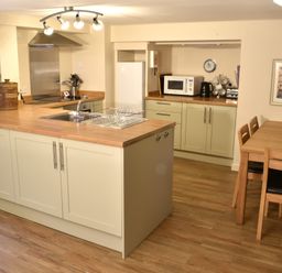 A kitchen with wooden countertops a dining table with chairs a microwave and a plant at Kingfisher in Blaenwaun