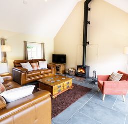 A living room with brown leather sofas a red armchair a wooden coffee table a wood-burning stove and a television at Hen Gelligemlyn - The Annexe in Ganllwyd