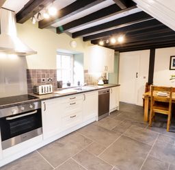 A kitchen with white cabinets a stove a toaster a kettle a sink a dining table with chairs and flowers at Hen Gelligemlyn - The Annexe in Ganllwyd