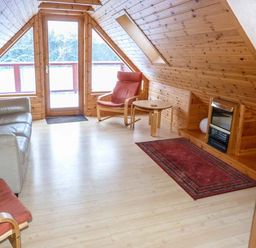 A living room with wooden walls a sofa chairs and a rug at Strathavon Chalet in Aviemore