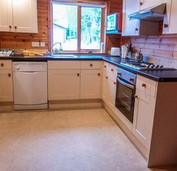 A kitchen with white cabinets dishwasher oven stovetop microwave and window at Strathavon Chalet in Aviemore
