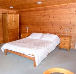 A bedroom with a double bed a wooden wardrobe two bedside tables with lamps and wooden walls at Strathavon Chalet in Aviemore
