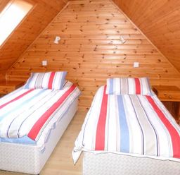A bedroom with two single beds with striped bedding and wooden nightstands under a slanted wooden ceiling at Strathavon Chalet in Aviemore