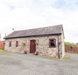 A stone cottage with a wooden door and four windows surrounded by flower pots and hanging planters at Bwthyn Ty Newydd in Llangadfan