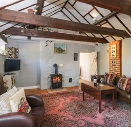 A living room with exposed wooden beams a wood stove a patterned rug leather sofas and a wooden coffee table at Old Cart Shed Lyneham near Royal Wootton Bassett