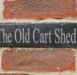 A sign reading The Old Cart Shed mounted on a brick wall at The Old Cart Shed in Lyneham near Royal Wootton Bassett