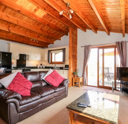 A living room with a brown leather sofa and kitchen area with white cabinets and black appliances at Bittern Lodge in Tattershall Lakes Country Park