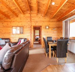 A wooden interior living room with leather sofas and a dining table with chairs at Bittern Lodge in Tattershall Lakes Country Park