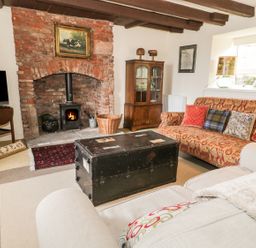A living room with a brick fireplace a wood stove a patterned sofa a beige sofa a TV and a black trunk coffee table at The Lookout in Berwick-upon-Tweed