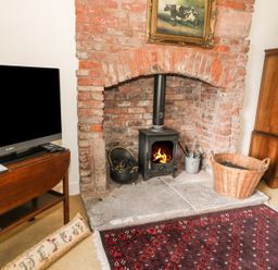 A room with a brick fireplace and wood-burning stove next to a television on a wooden table at The Lookout in Berwick-upon-Tweed