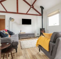A living room with two grey sofas a wood stove and a television mounted on the wall at The Stable in Berkeley