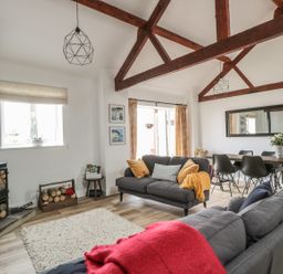 A living room with wooden beams on the ceiling two grey sofas and a dining table with black chairs at The Stable in Berkeley