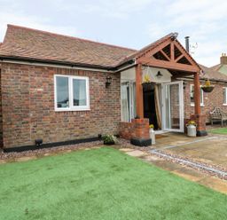A single-story brick house with a tiled roof an open glass door a wooden porch hanging flower baskets green artificial turf and a paved patio area at The Stable in Berkeley