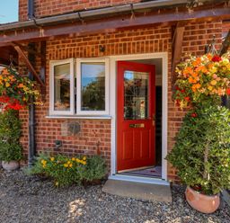 A front entrance with a red door surrounded by hanging flower baskets and potted plants at Camerons Cottage in Swaffham