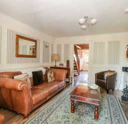 A living room with a leather sofa a wooden coffee table and a fireplace at Camerons Cottage in Swaffham