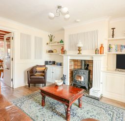A living room with a fireplace a coffee table an armchair a TV and shelves at Camerons Cottage in Swaffham
