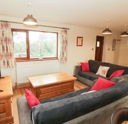 A living room with two grey sofas red and floral cushions a wooden coffee table and TV on a wooden stand at Bodneithior in Llanerchymedd