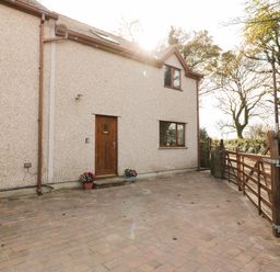 A paved driveway with a wooden gate and a beige house with wooden door and windows at Bodneithior in Llanerchymedd