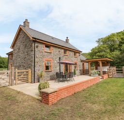 A stone farmhouse with a patio table and chairs under an umbrella and a covered hot tub in a garden at The Farmhouse in Capel Bangor near Aberystwyth