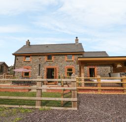 Exterior view of a stone house with a patio table umbrella wooden fence and covered hot tub at The Farmhouse in Capel Bangor near Aberystwyth
