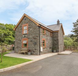 A stone house with a bench and potted plants outside near trees and a gate at The Farmhouse in Capel Bangor near Aberystwyth