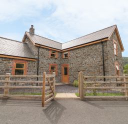 A stone house with wooden framed windows and a wooden gate in front at The Farmhouse in Capel Bangor near Aberystwyth